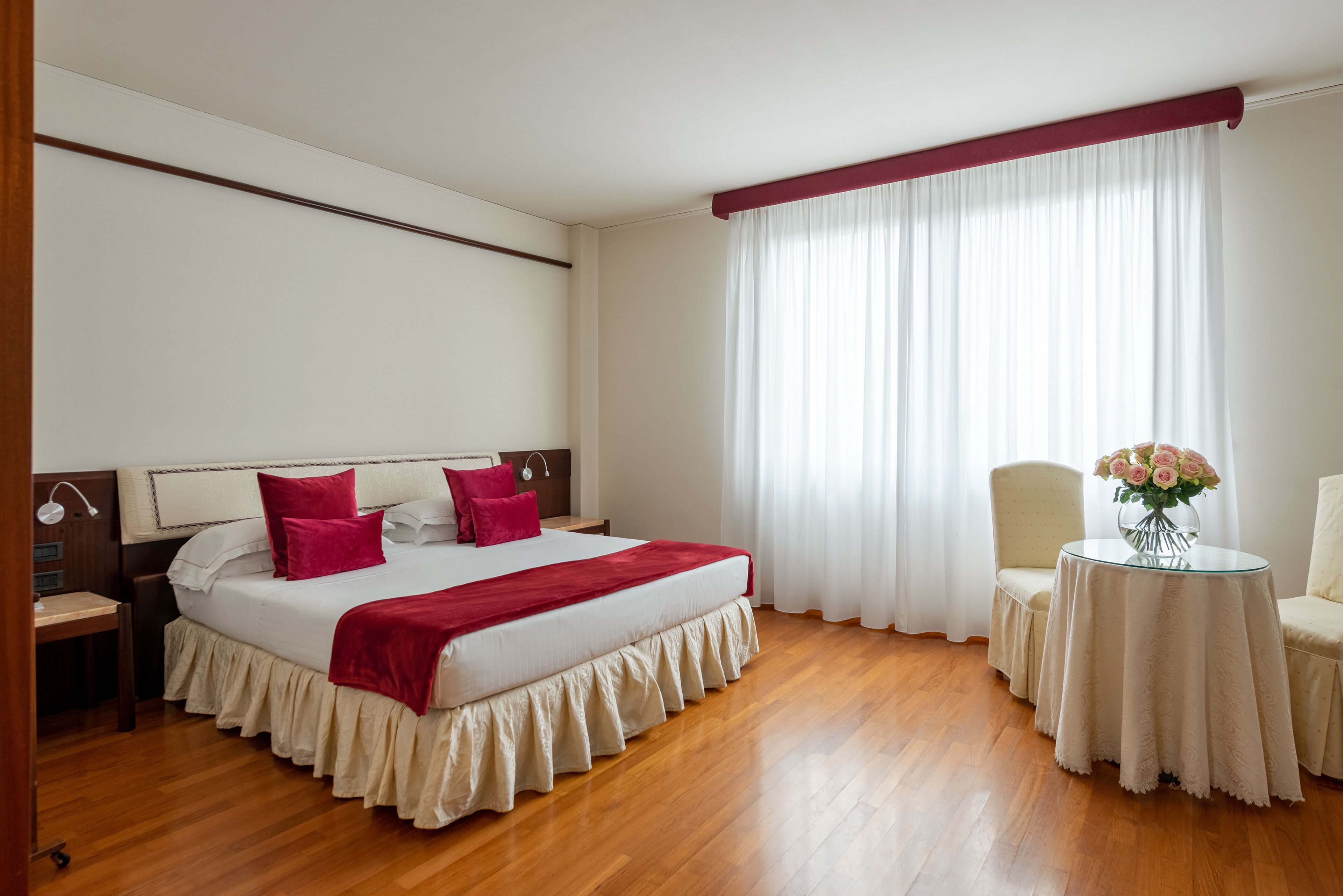 A hotel room with a large bed, a desk, a chair, and a small table with a vase of flowers.