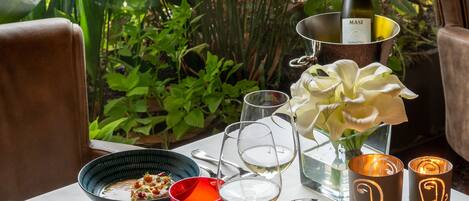A dining table set with plates, glasses, a wine bottle, a candle, and a basket of pastries.