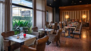 Ein Hotel-Rezeptionsbereich mit einem Schild, auf dem 'HOTEL LEOPARDI RECEPTION' steht, Tischen zum Essen und Blick auf Grünfläche vor dem Haus.