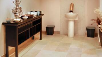 A hallway with a dark wooden console table, a white pedestal sink, and two black trash bins.
