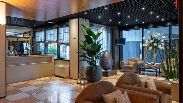 Eine moderne Lobby mit einer Rezeption, einer Sitzecke, großen Fenstern und dekorativen Pflanzen.