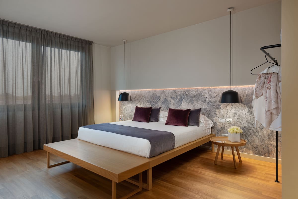 A modern bedroom with a bed, bedside tables, a bench, a hanging light, and a wall-mounted lamp.