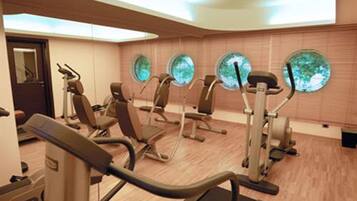 A gym with exercise equipment, including treadmills and stationary bikes, and large windows with a view of trees.