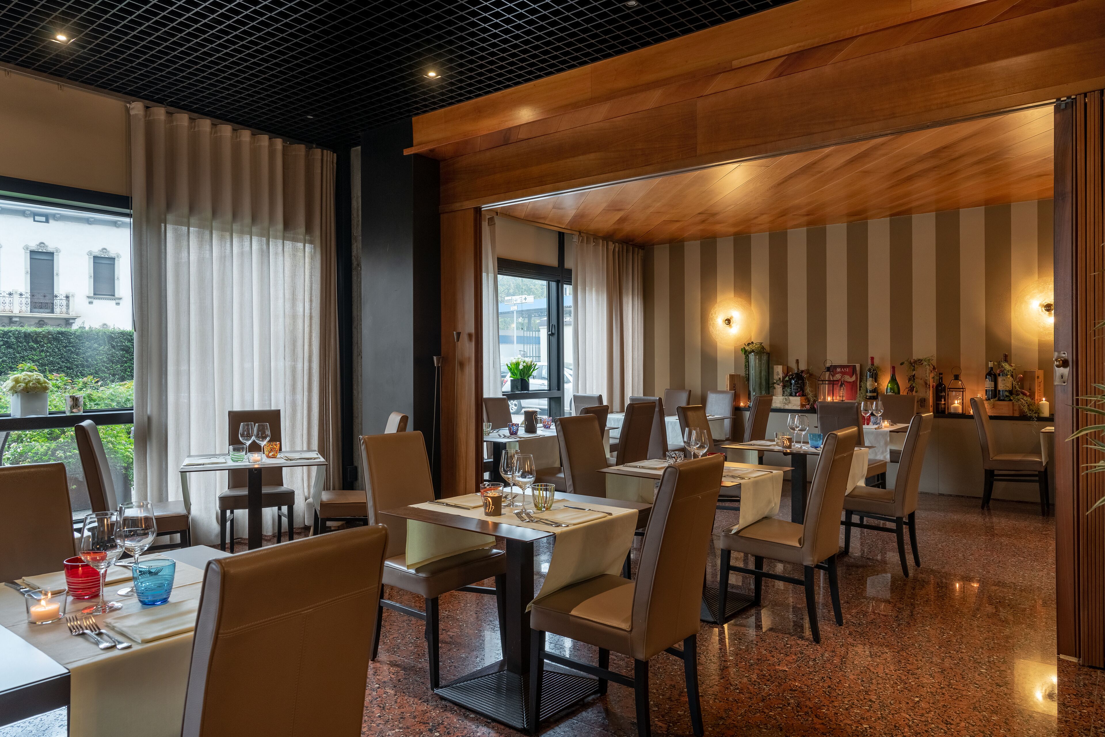 Un restaurant avec des tables dressées, des chaises et une vue sur l’extérieur.