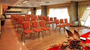 Una sala conferenze con file di sedie arancioni, un pavimento in legno e un tavolo rosso con un'esposizione floreale.