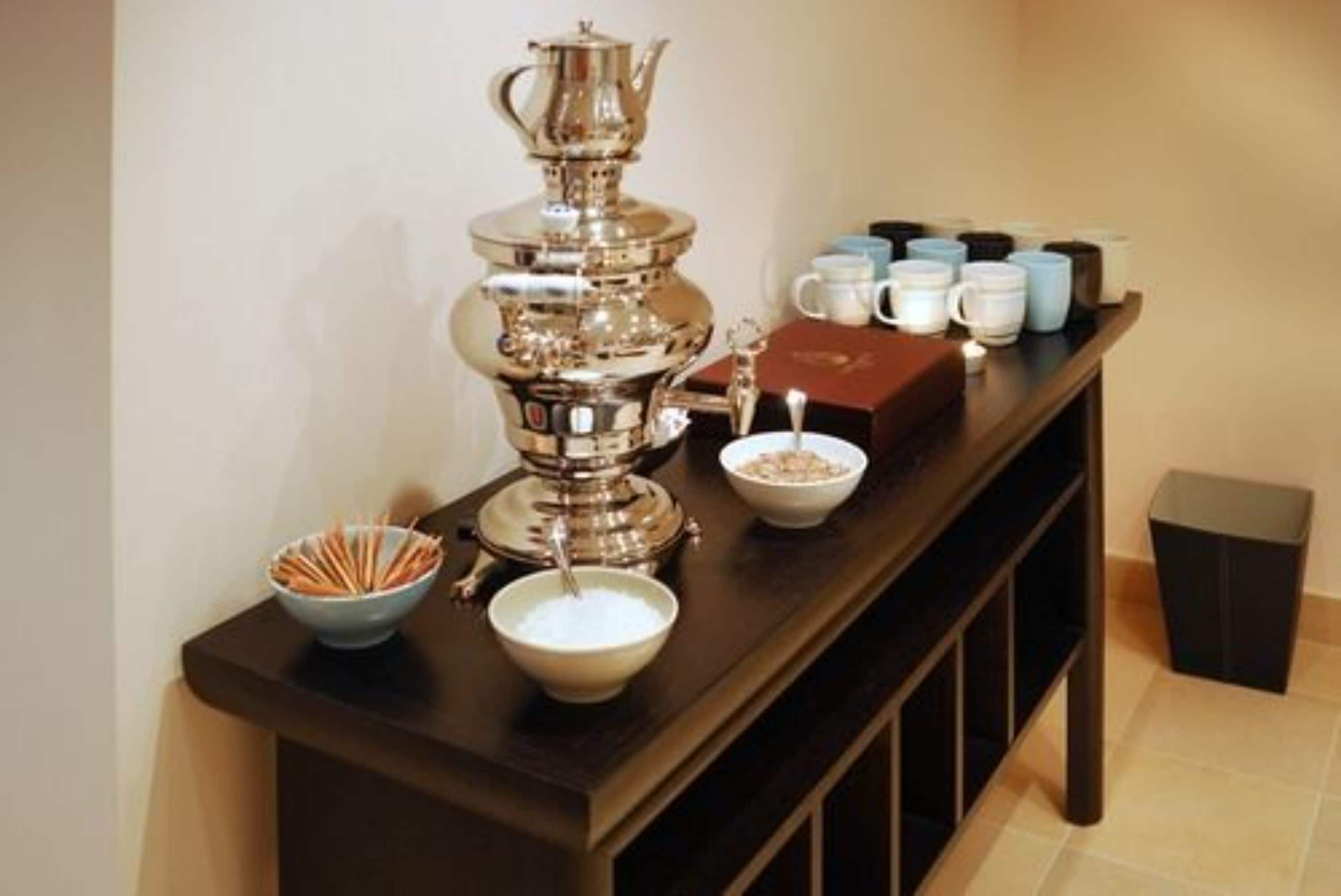 A buffet setup with a silver teapot, bowls of food, and various mugs on a wooden table.