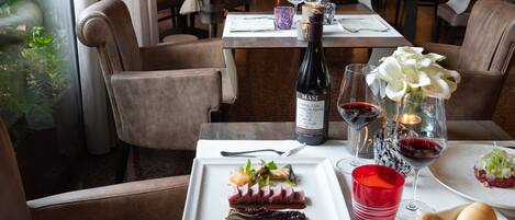 A dining table set with a bottle of Masi wine, red wine glasses, a red cup, a plate of food, and a basket of bread.