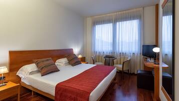 Habitación de hotel con una cama grande, un escritorio con computadora, una silla y un televisor.