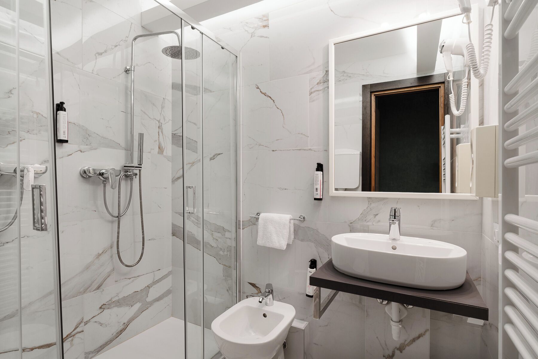 Un baño moderno con ducha de vidrio, lavamanos pedestal y un bidé.