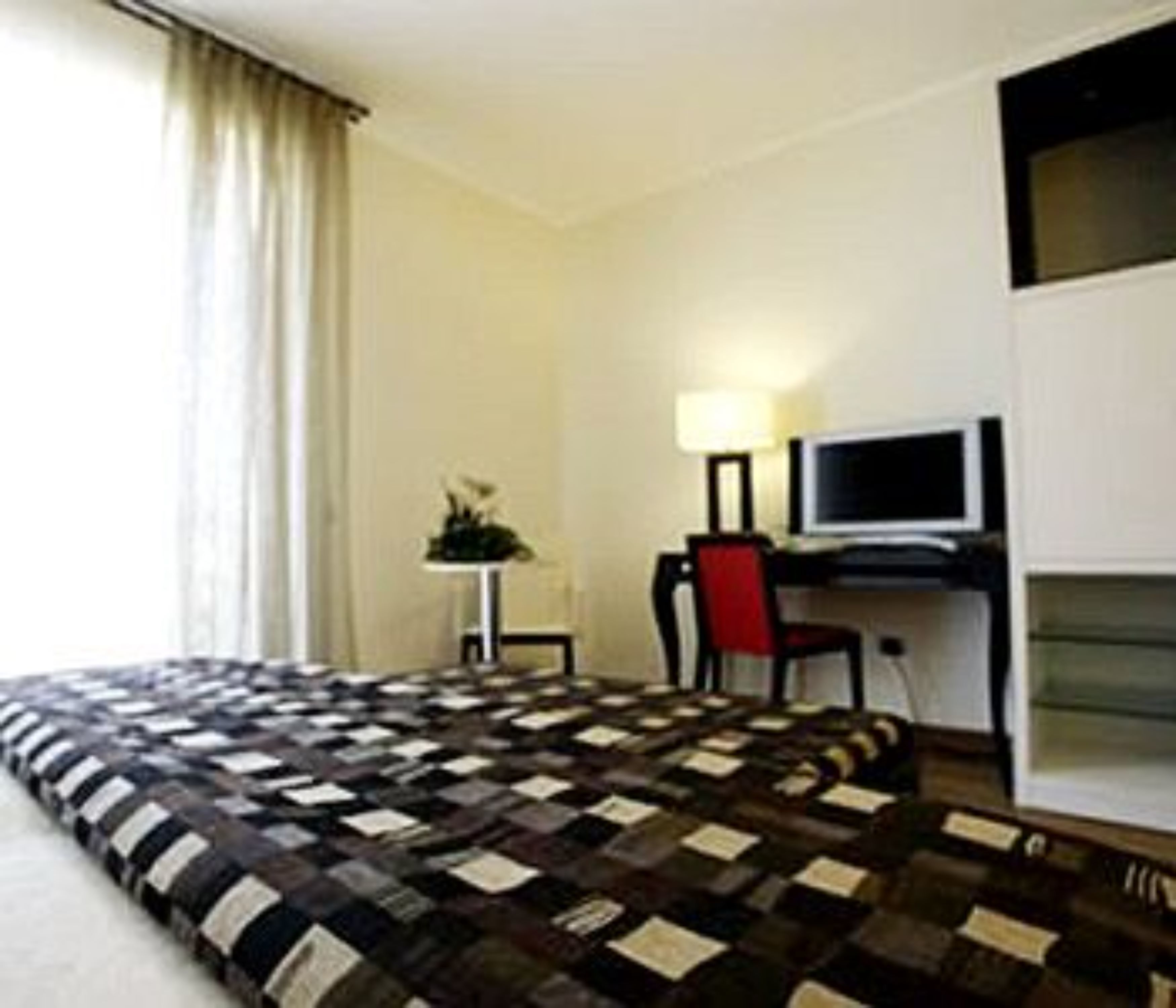 Une chambre d’hôtel avec un grand lit, un bureau avec un ordinateur, une chaise et une petite table avec une lampe.