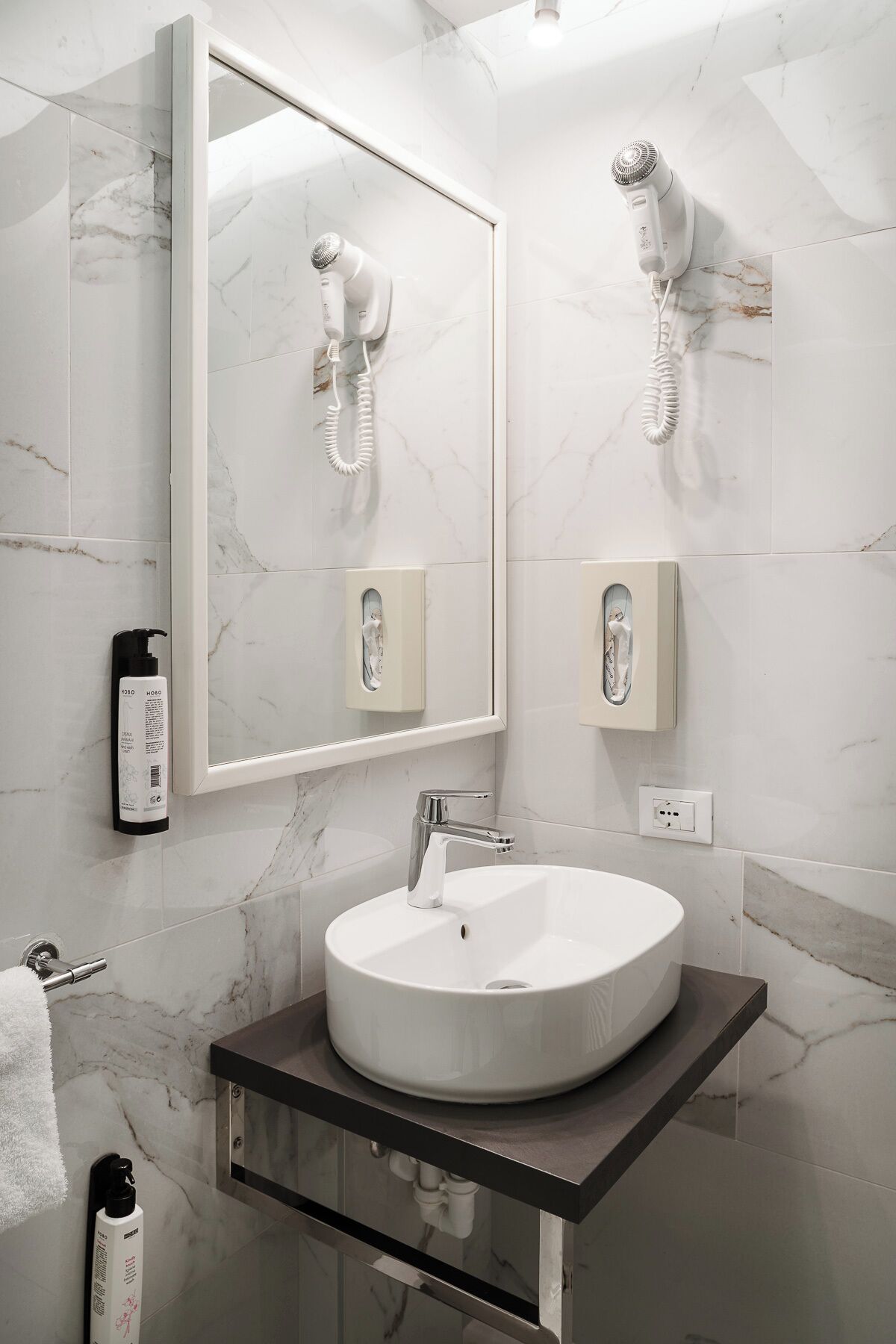 Un baño moderno con un espejo grande, un lavabo redondo y dos secadores de pelo fijados a la pared.