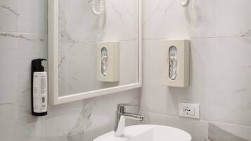 A modern bathroom with a large mirror, a round sink, and two wall-mounted hair dryers.