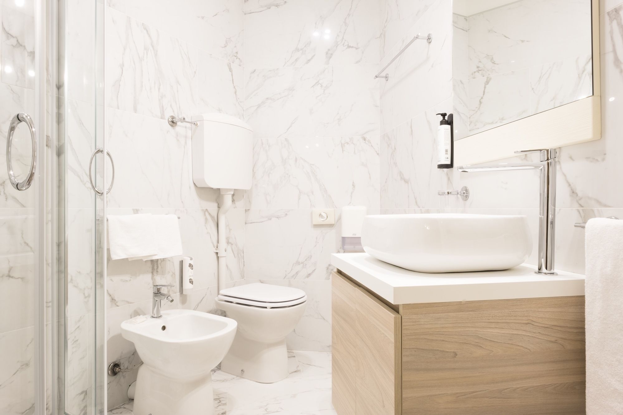 A modern bathroom with a marble backsplash, a freestanding sink, a bidet, and a toilet.