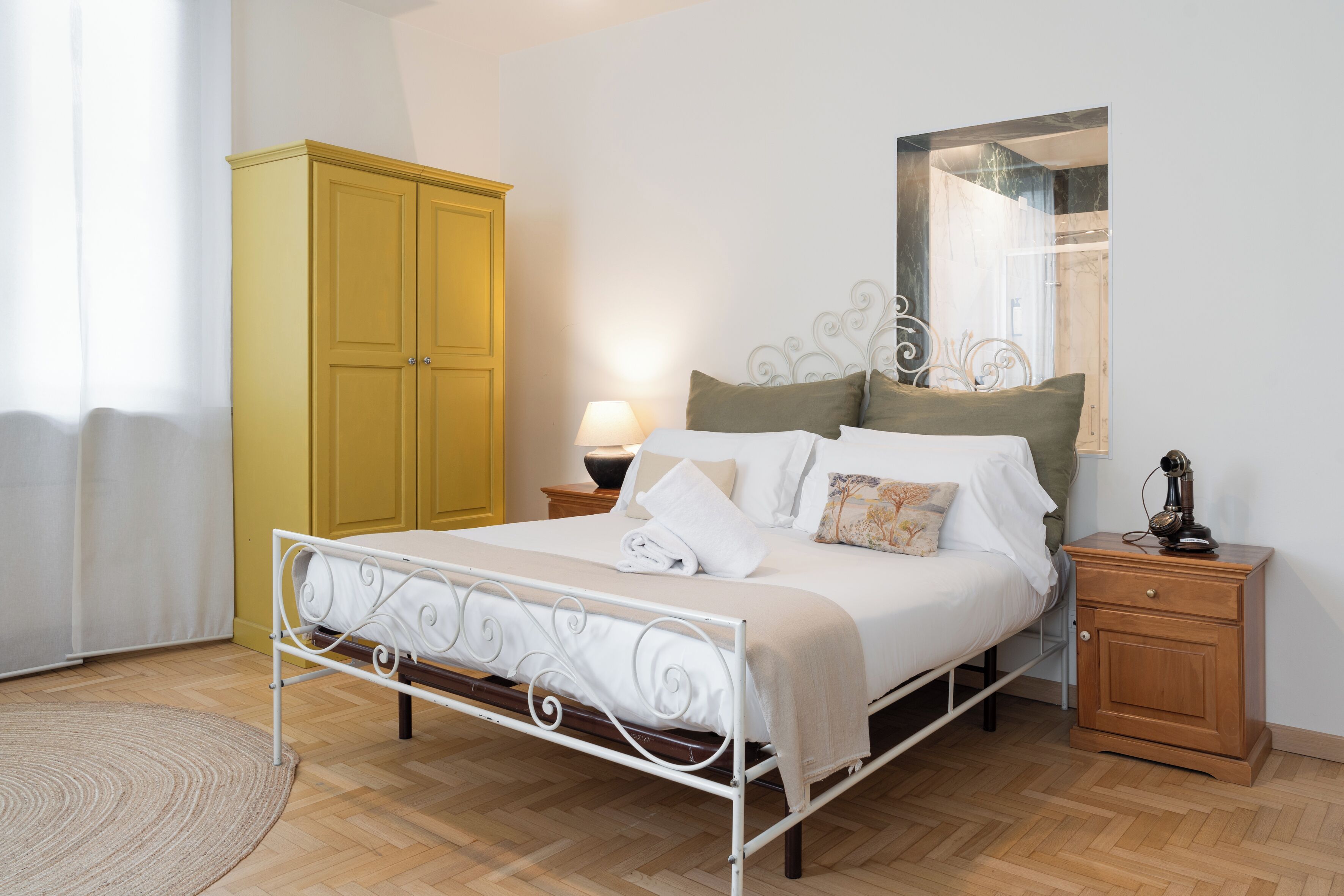 A bedroom with a bed, a nightstand, a wardrobe, and a mirror on the wall.