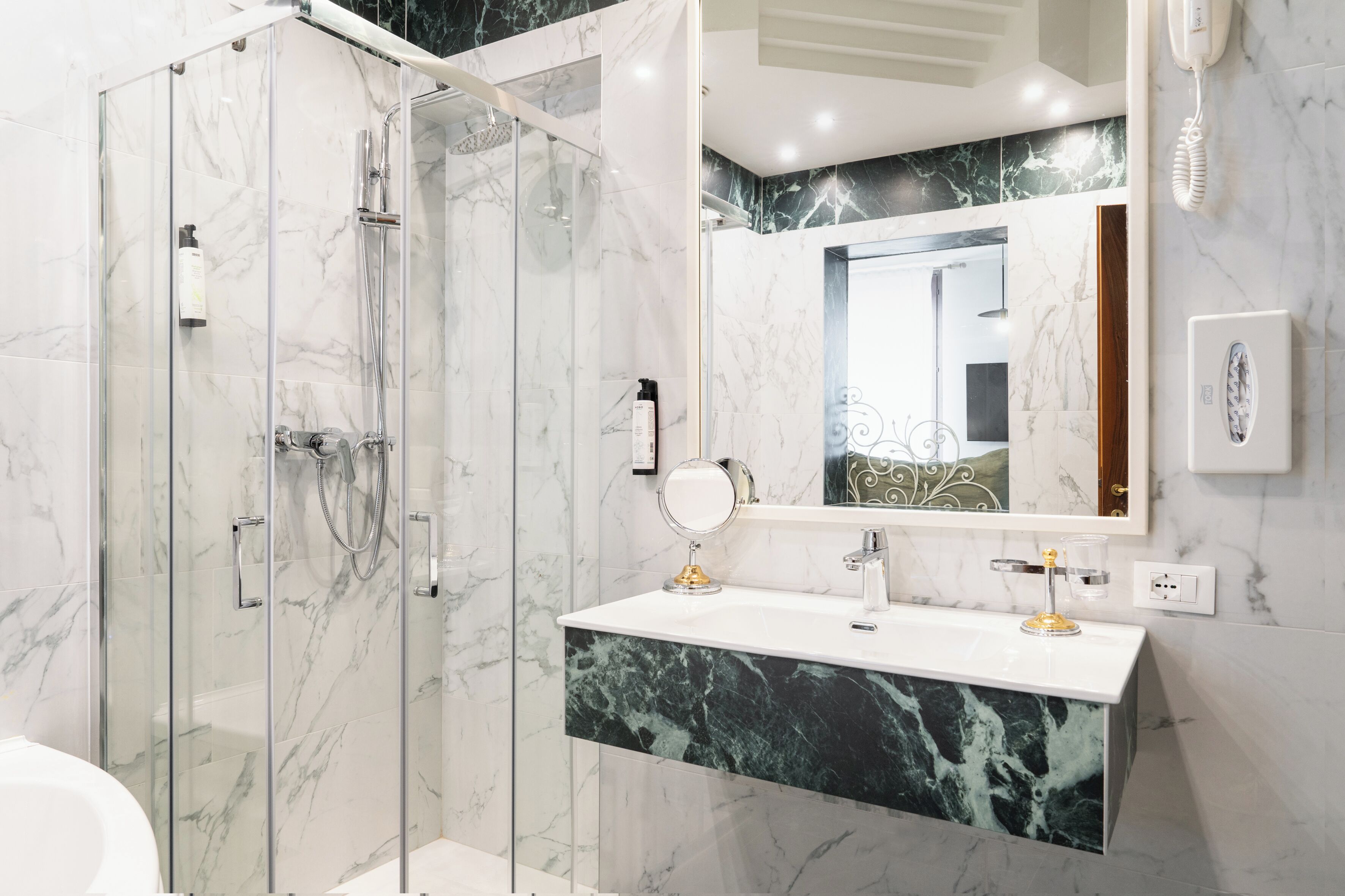 A modern bathroom with a glass-enclosed shower, a marble vanity, and a large mirror.