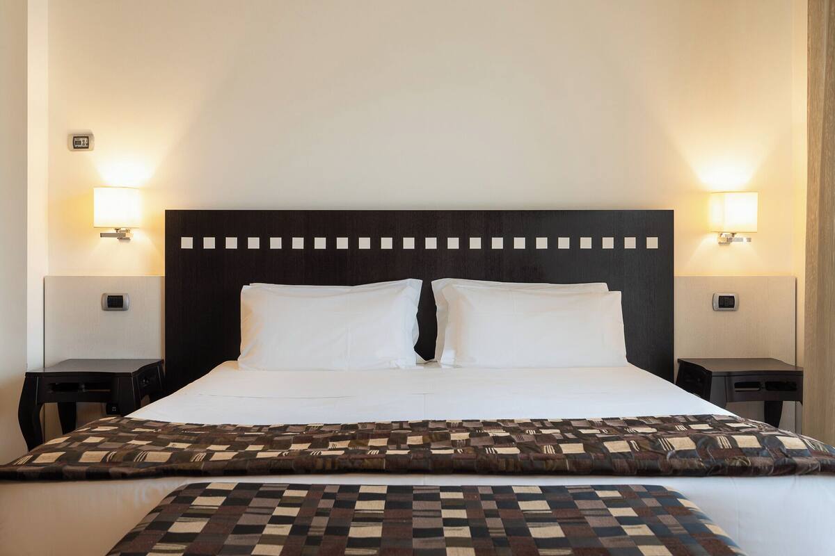 A hotel room with a large bed, two bedside tables, and wall-mounted lamps.