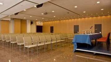A conference room with rows of chairs, a stage with a table and chairs, and a podium.