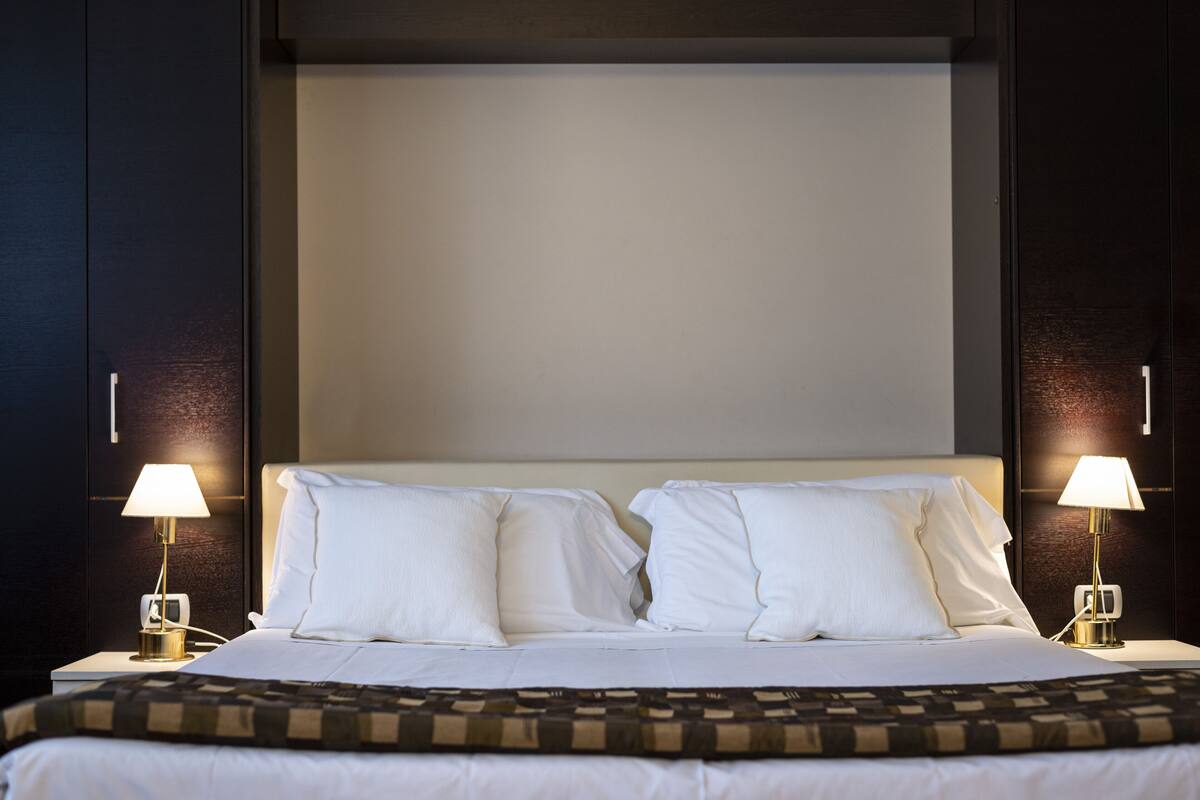 A neatly made bed with white linens and two bedside lamps.