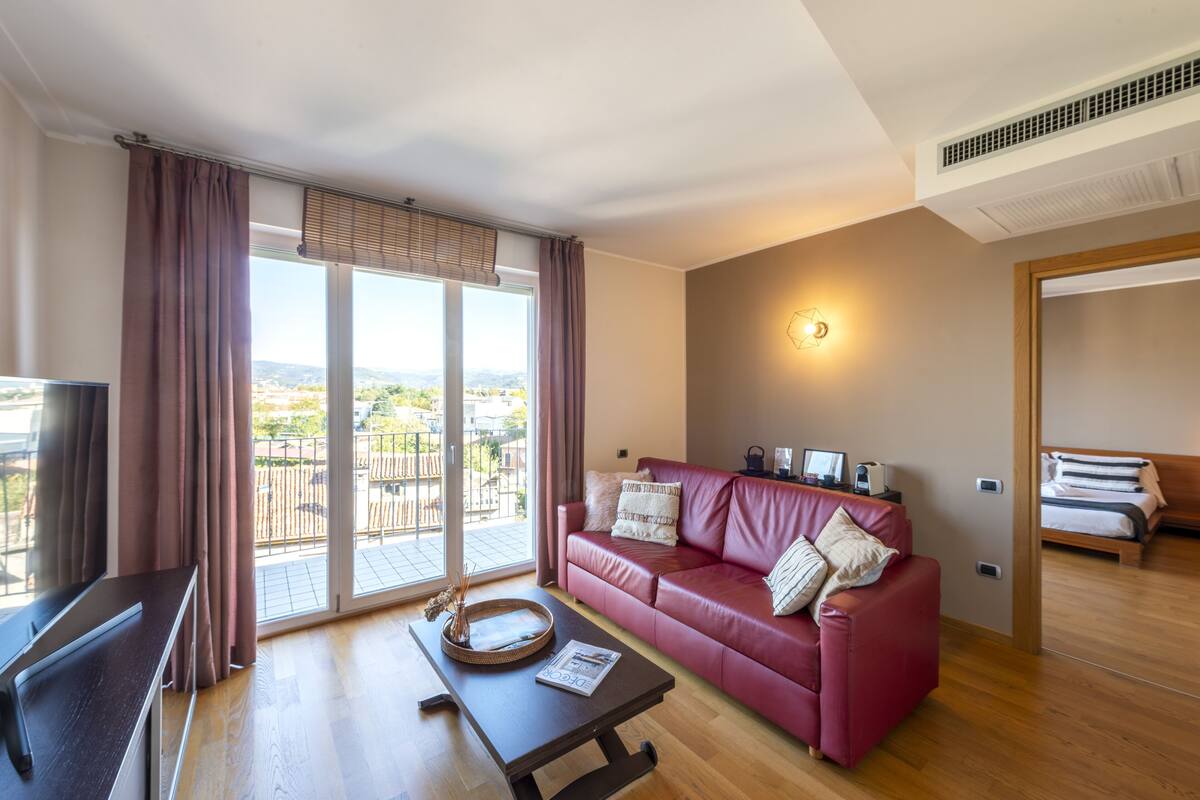 A modern living room with a red leather sofa, a wooden coffee table, a TV, and a large sliding glass door leading to a balcony.