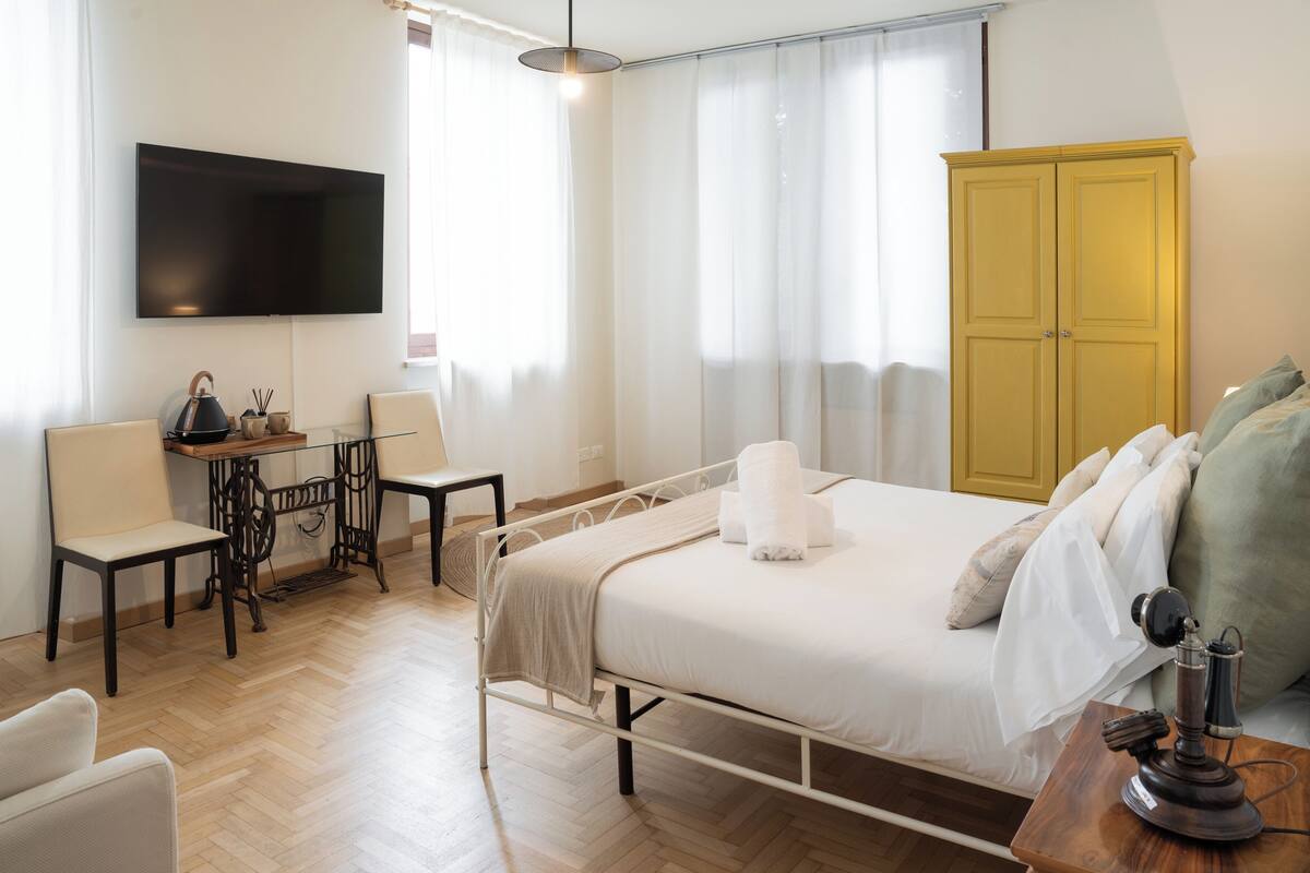 A hotel room with a bed, a desk, a chair, a television, and a wardrobe.