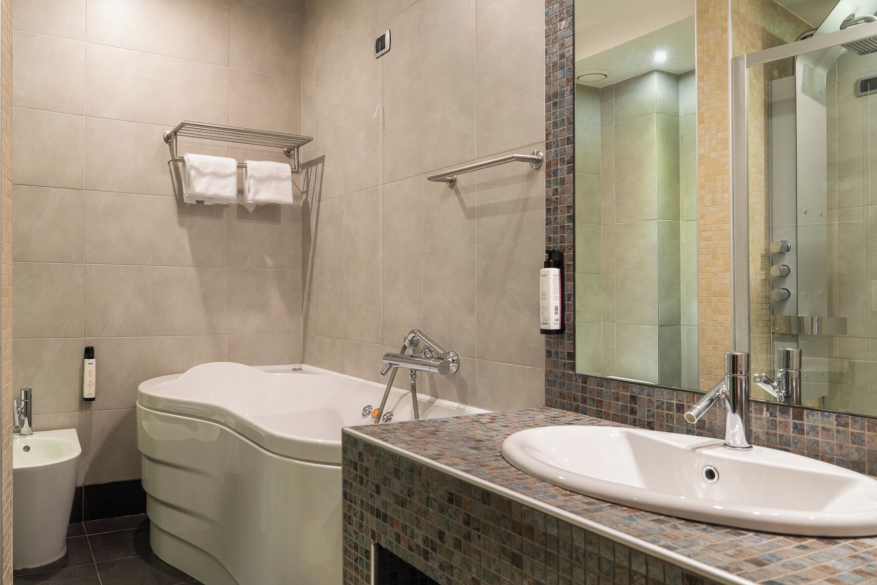 A modern bathroom with a bathtub, a sink, and a toilet. There is a towel rack above the bathtub and a mirror above the sink.