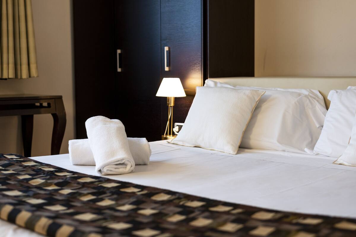 A neatly made bed with white linens and pillows, a bedside lamp, and a dark wooden door in the background.