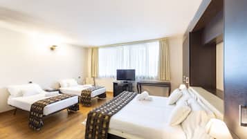 Una camera d'albergo con due letti singoli, un divano letto, una televisione e una scrivania.