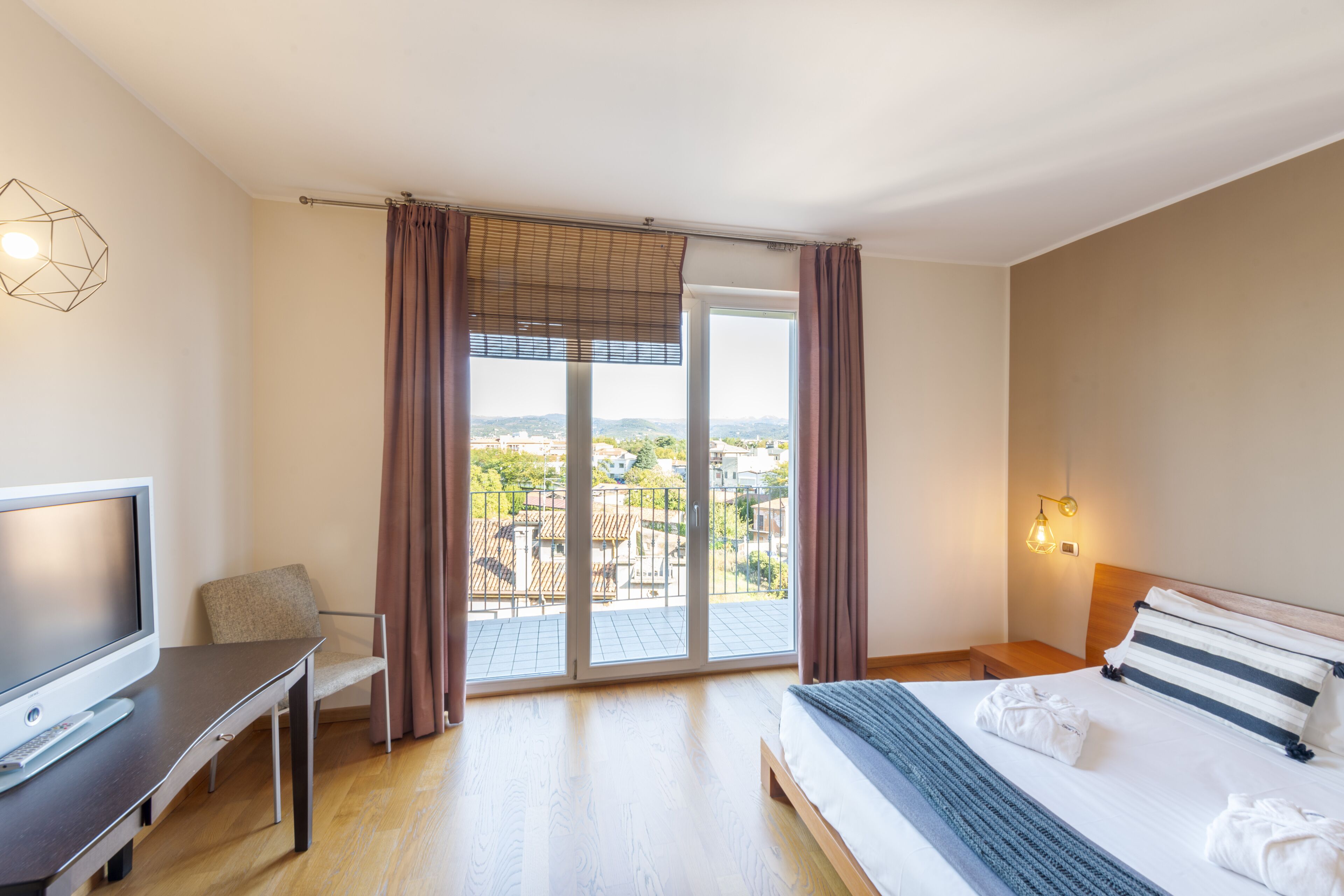 Ein Hotelzimmer mit Bett, Schreibtisch, Fernseher, Stuhl und Blick aus dem Fenster.