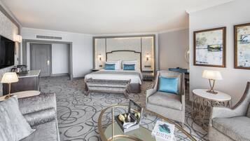 Une chambre d’hôtel avec un grand lit, deux fauteuils, une table basse, un téléviseur et des œuvres d’art accrochées aux murs.