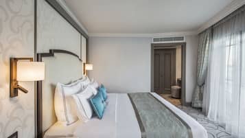 Une chambre d’hôtel avec un grand lit, deux lampes de chevet, une tête de lit dotée d’un luminaire, une petite table et une porte donnant sur une salle de bain.
