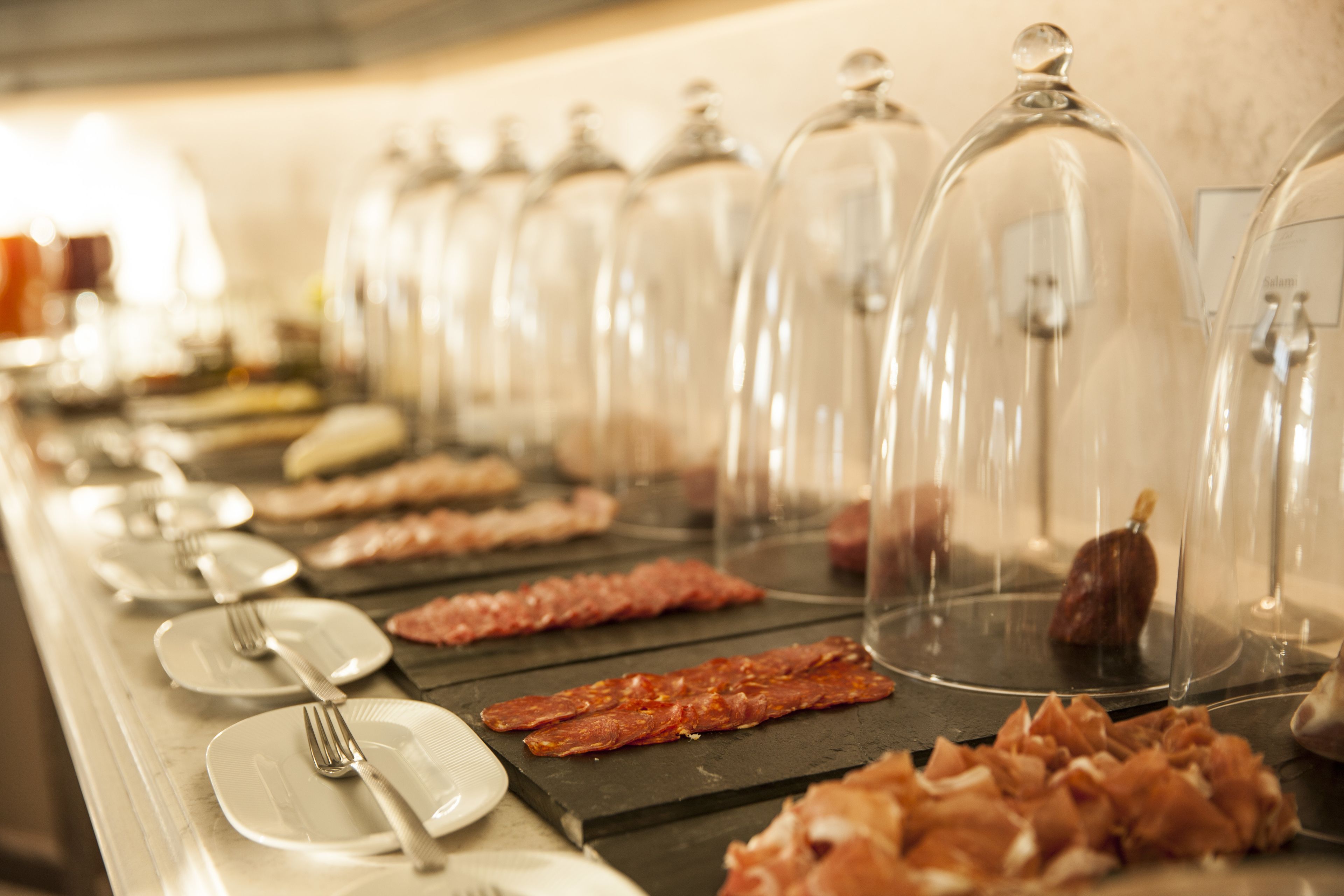 A buffet with various meats under glass domes, plates, and cutlery.