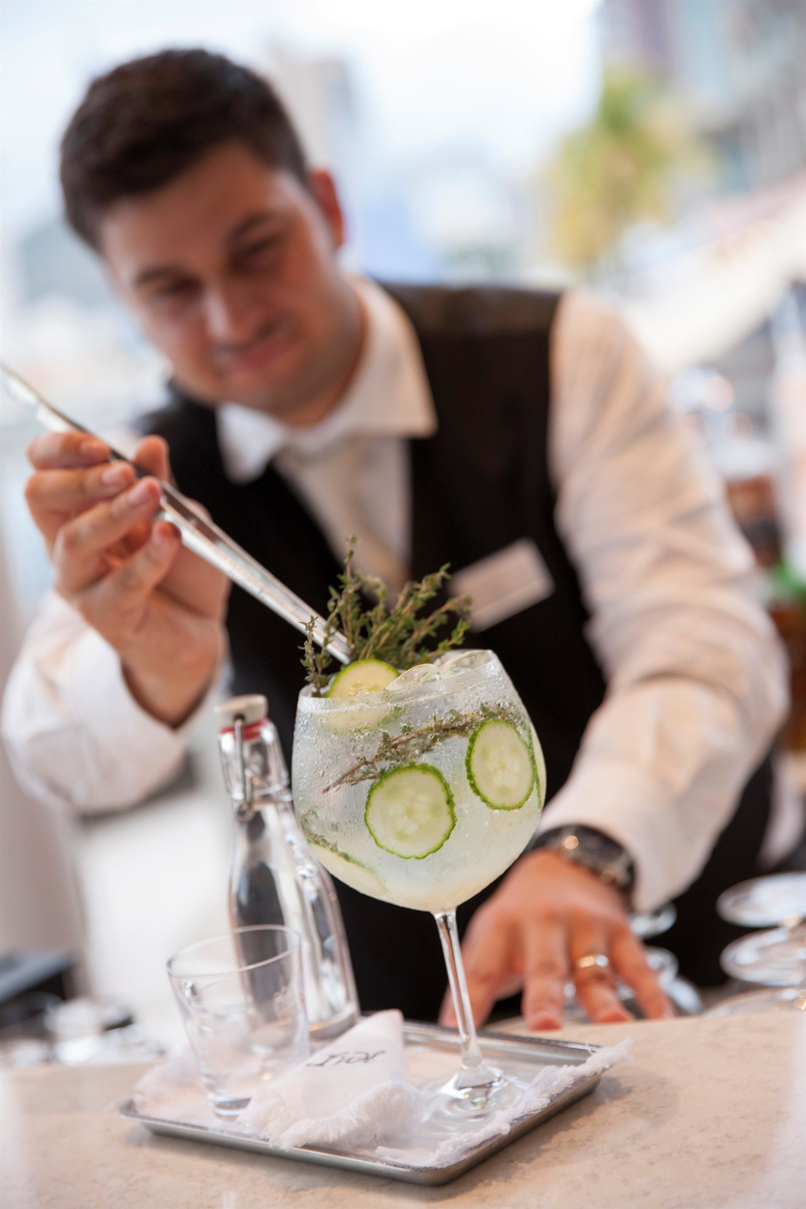 En bartender som blandar en cocktail och har ett glas på ett bricka.