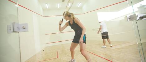 A squash court with wooden flooring and glass walls.