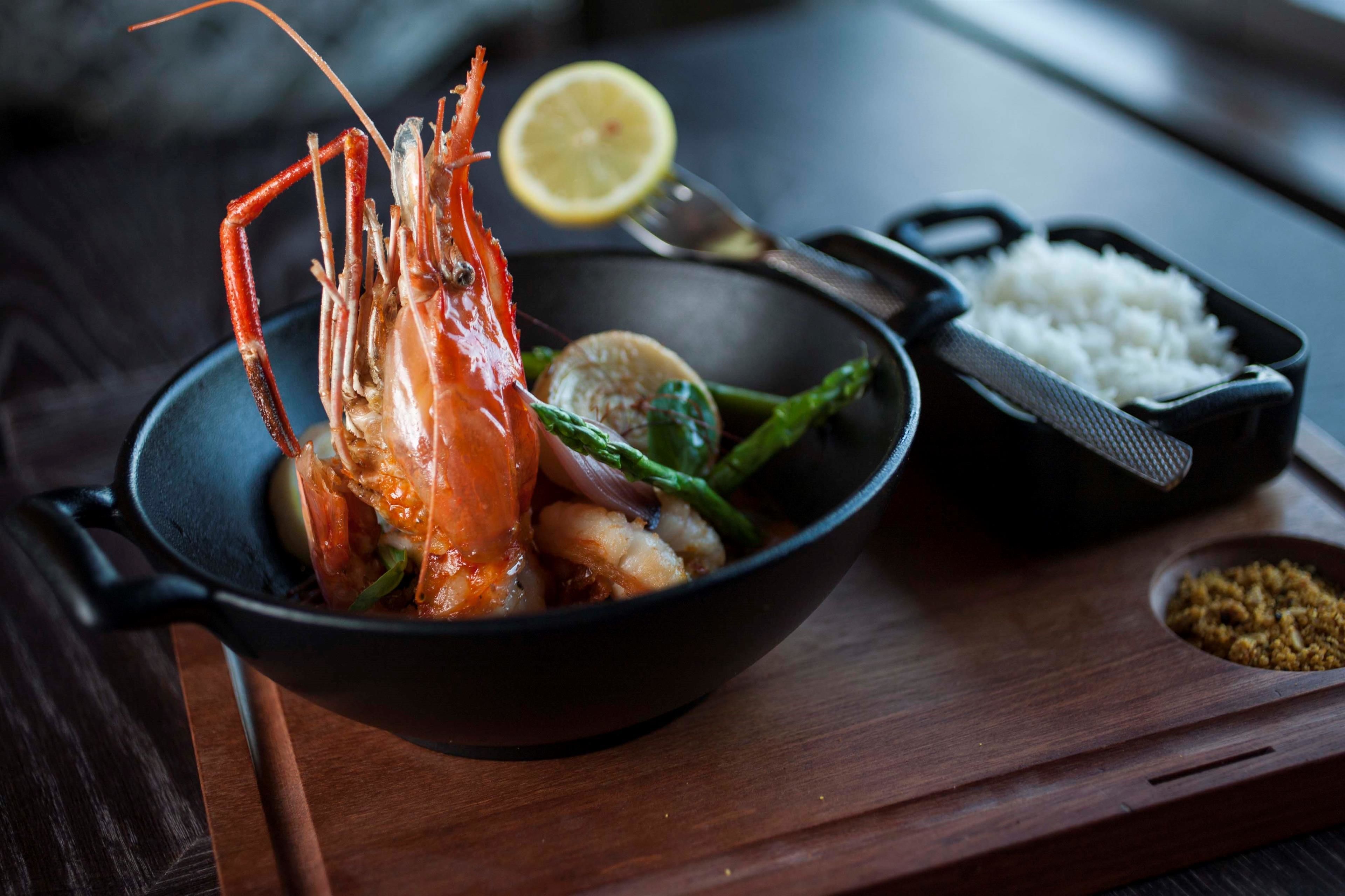 A bowl of seafood with a lobster, lemon, and rice on a wooden board.