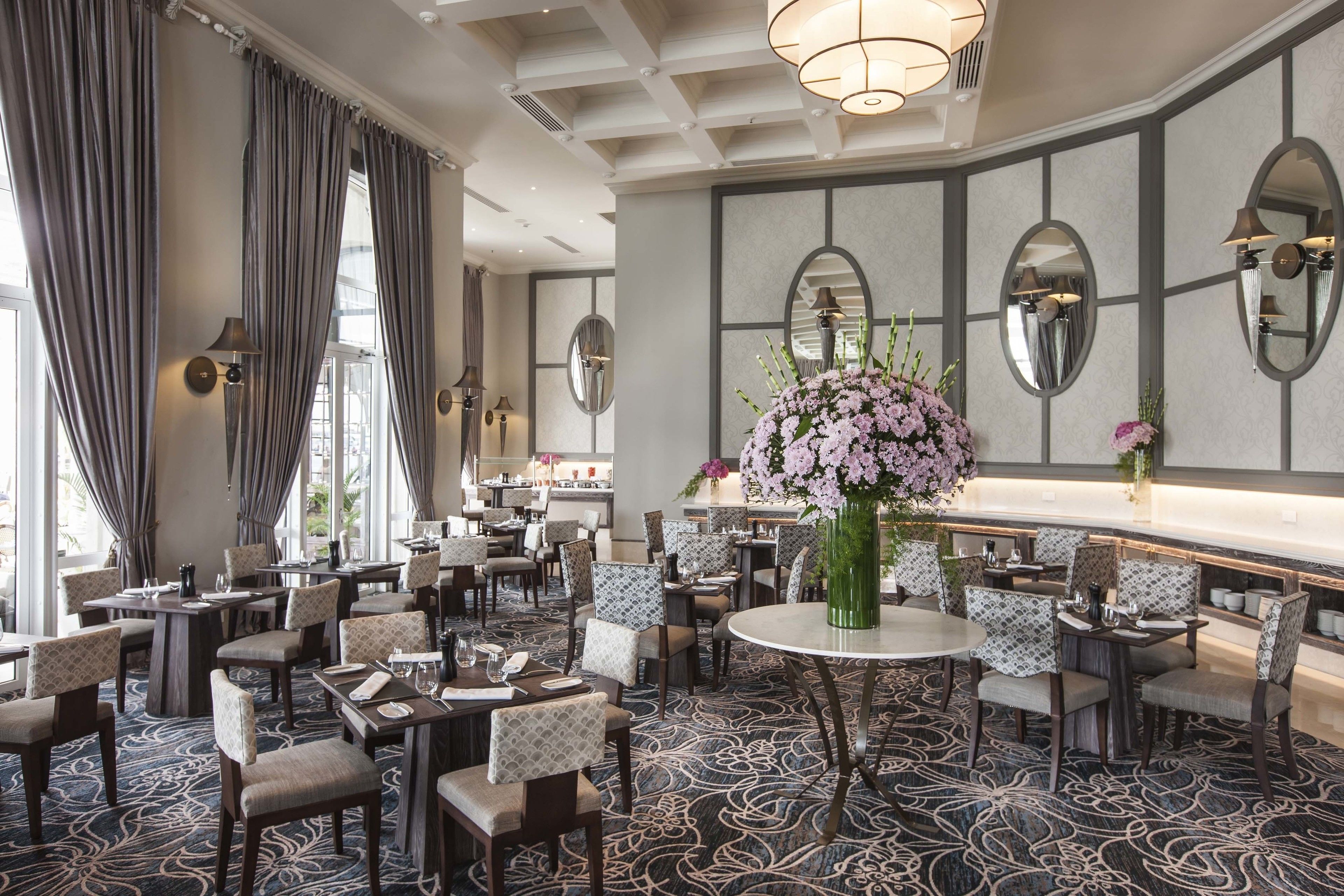 Un comedor de hotel con mesas redondas, sillas estampadas y un gran centro de mesa floral.