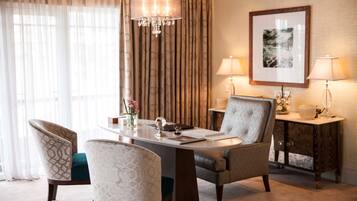 Une chambre d’hôtel comprenant une table à manger, deux chaises, un lustre, une table d’appoint avec une lampe et un tableau encadré au mur.