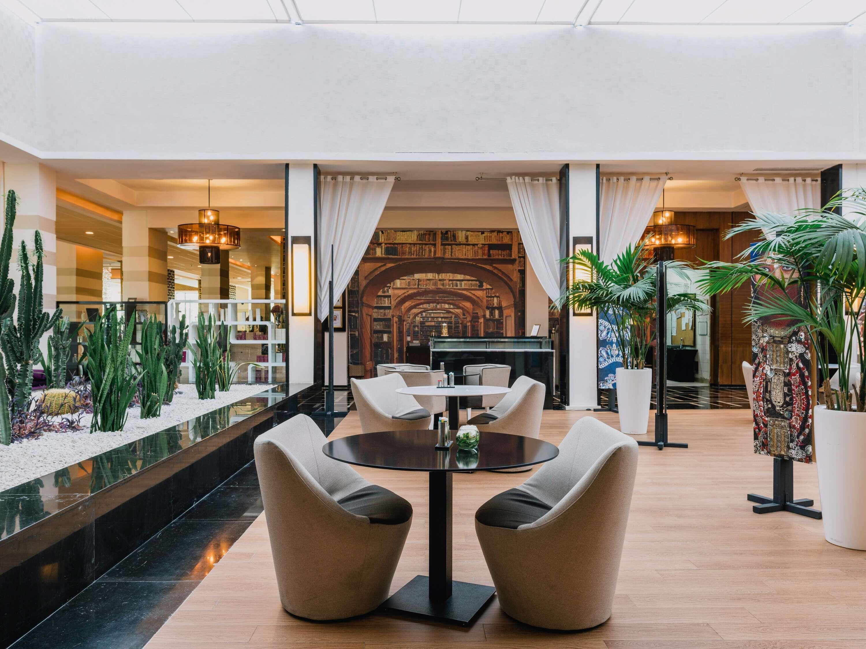A lobby with a round table, two armchairs, a bookshelf, and a potted plant.