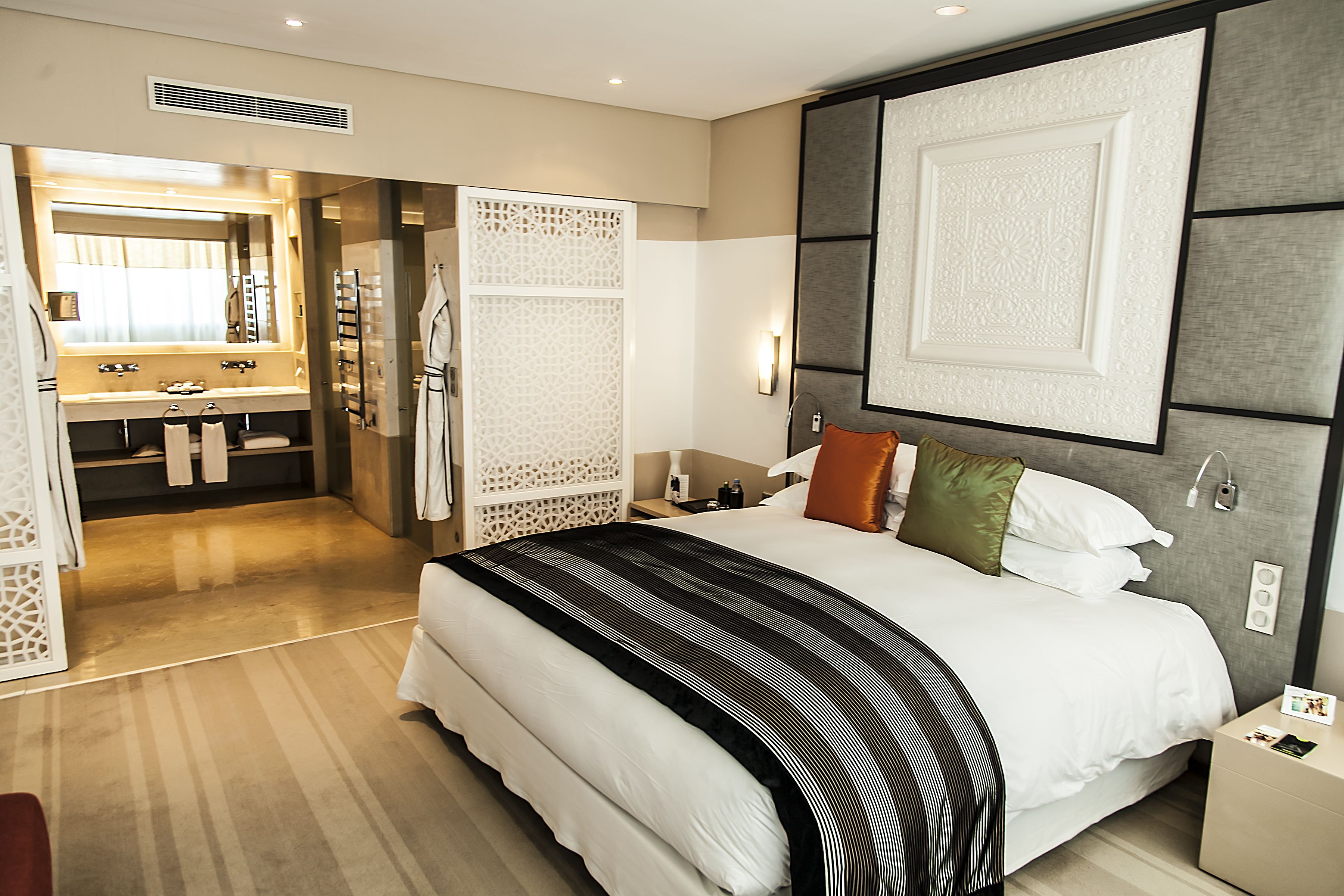 A modern hotel room with a large bed, a separate bathroom with a vanity, and a walk-in closet.