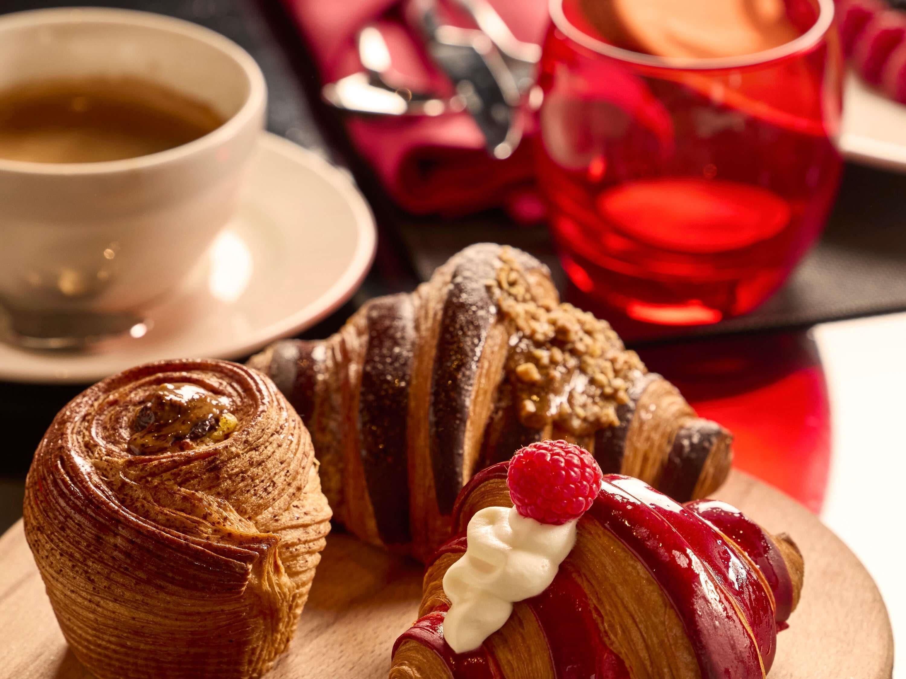 A pastry with a raspberry on top, a rolled pastry, and a cup of coffee.