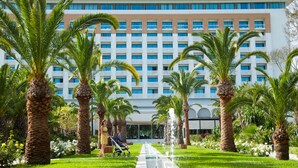 Un hotel amb façana moderna, palmeres i una font central.