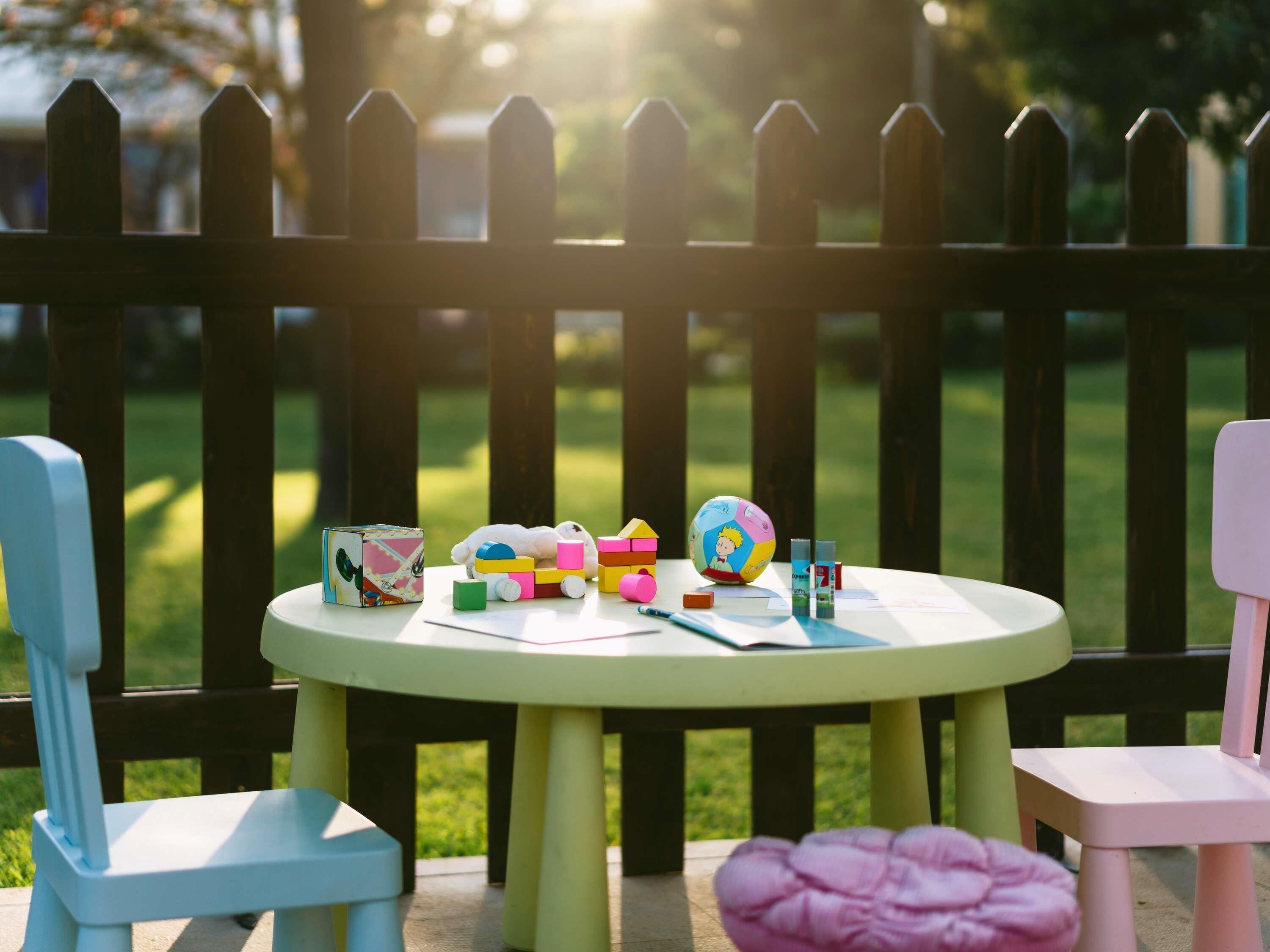 A round table with educational toys and books, surrounded by a wooden fence and chairs.