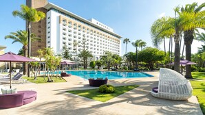 Hotel amb piscina, zones d'estar a l'exterior i palmeres.