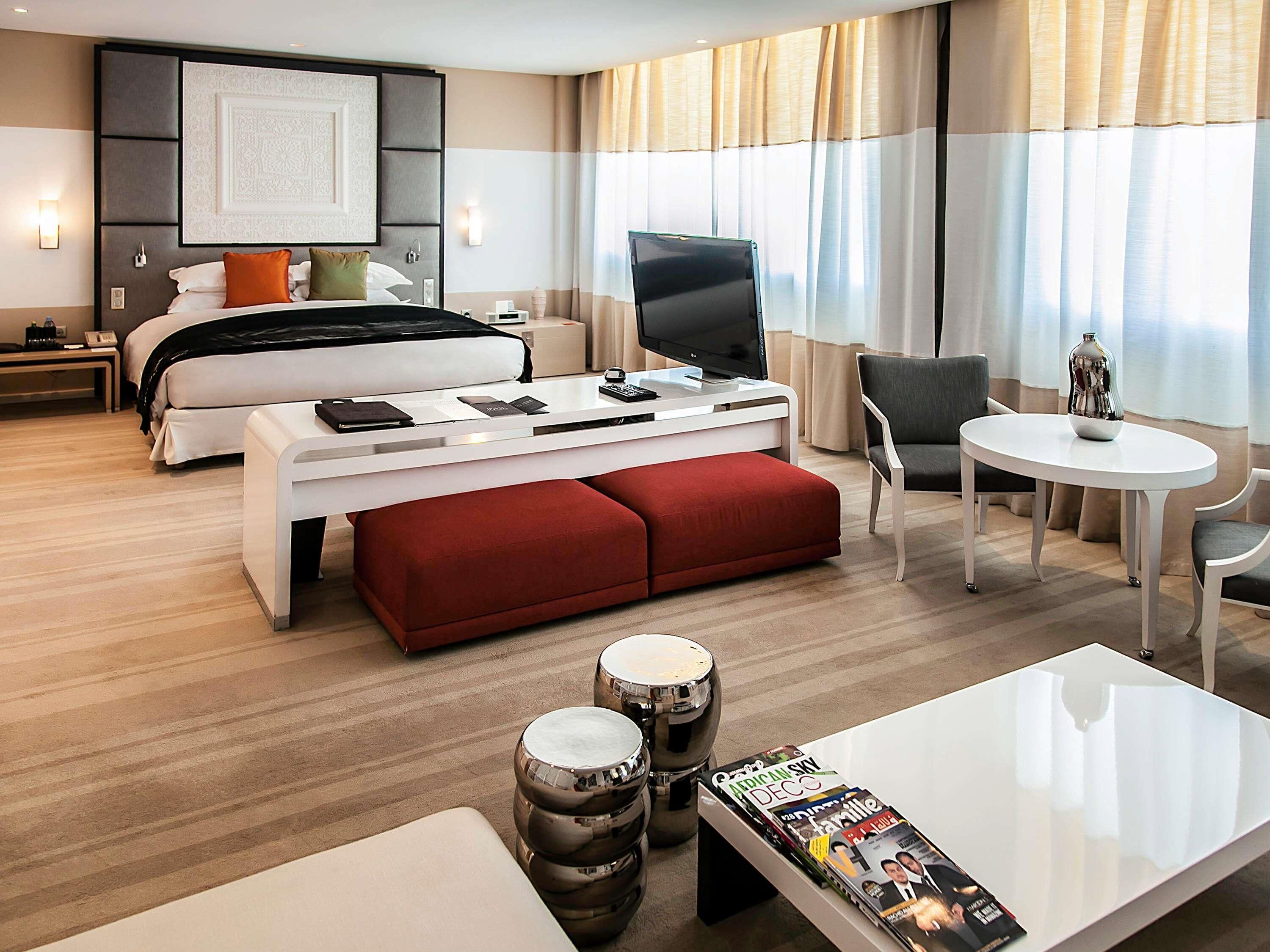 A modern hotel room with a bed, a desk, a TV, a dining table, and a magazine.