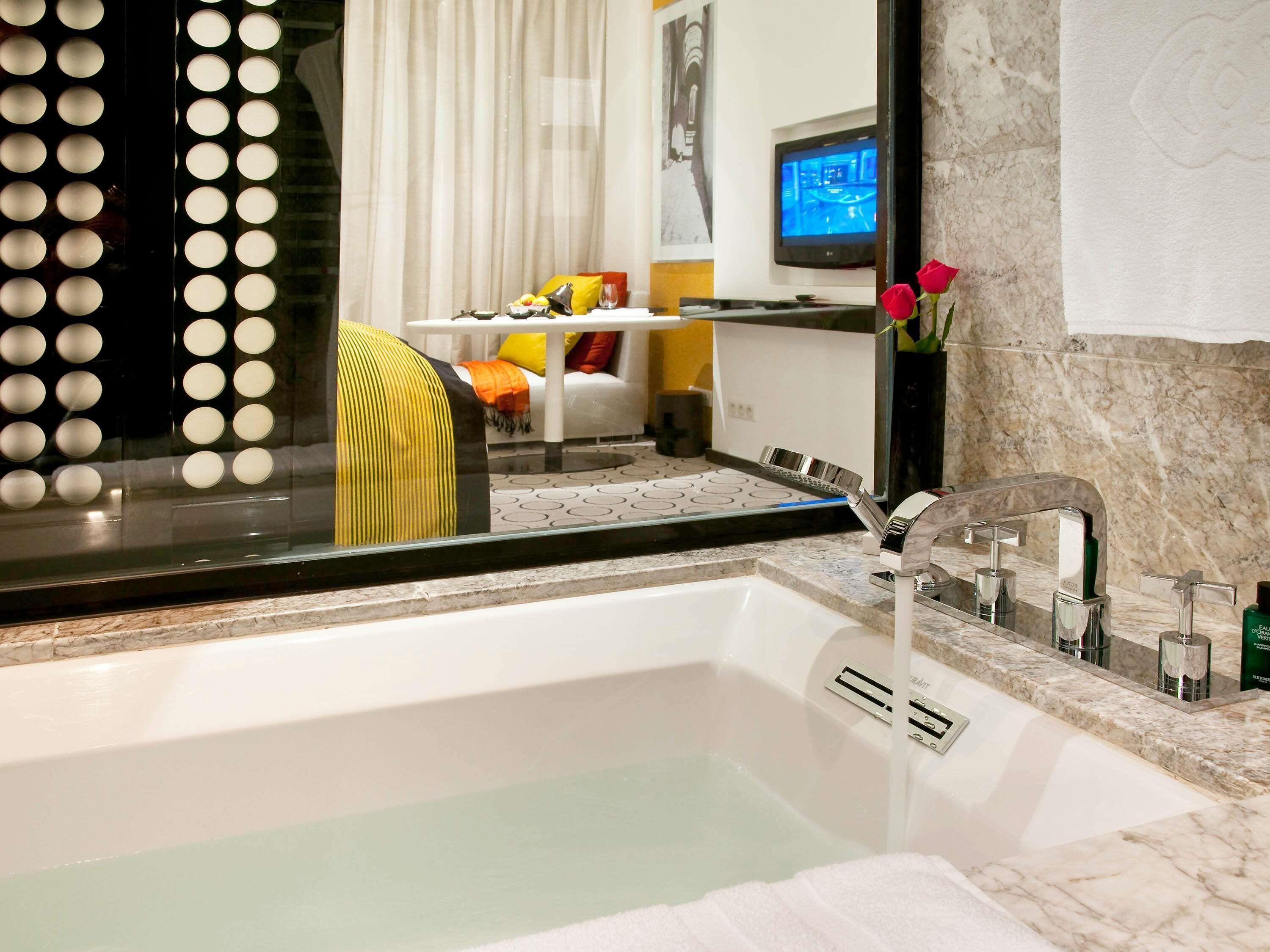 Ein modernes Badezimmer mit einer Badewanne, einem Spiegel und einem Fernseher im Hintergrund.