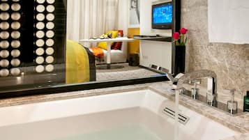 Ein modernes Badezimmer mit einer Badewanne, einem Spiegel und einem Fernseher im Hintergrund.