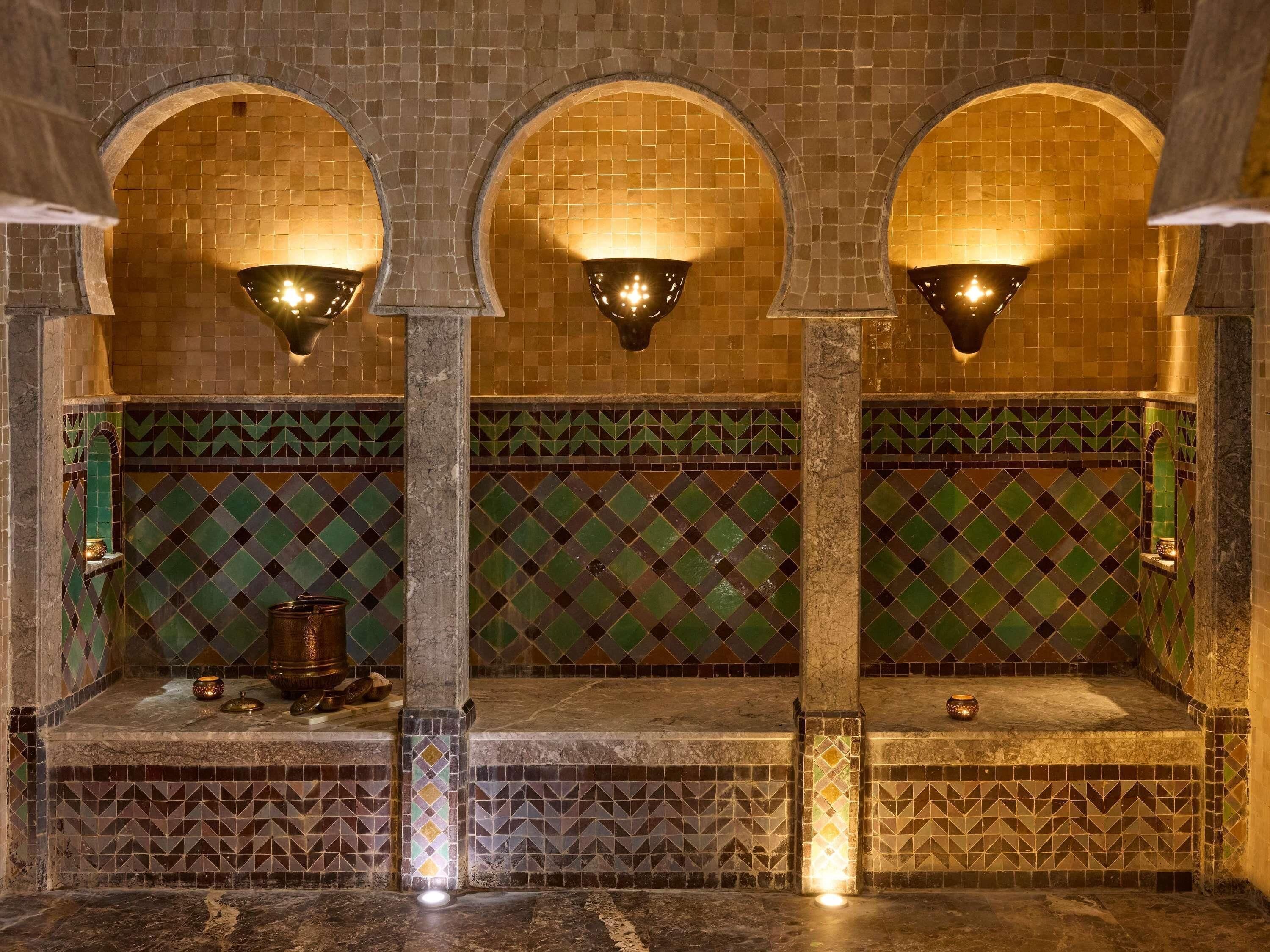 Un baño con azulejos, tres arcos, un banco de mármol e iluminación empotrada.
