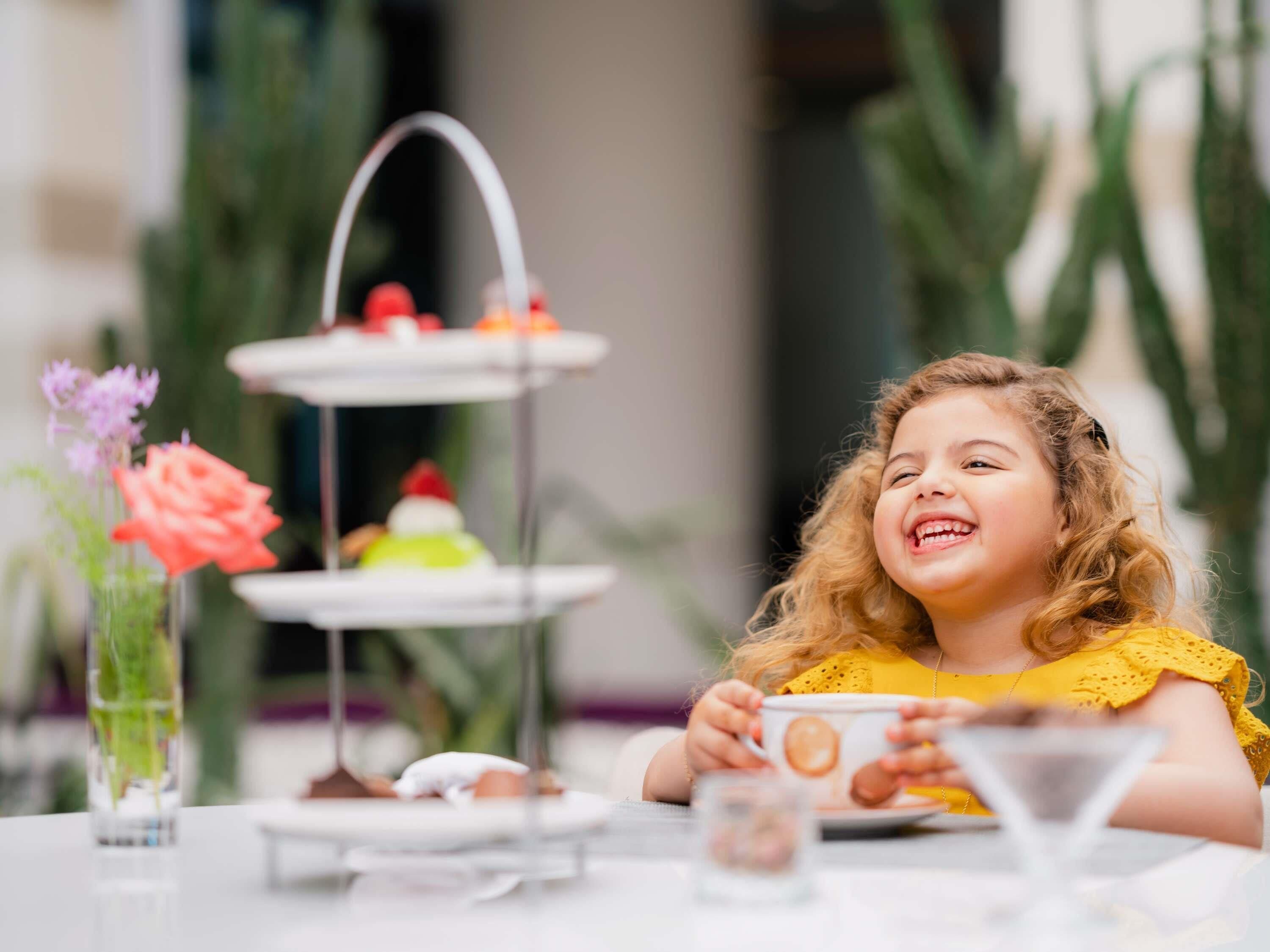 A child at a table with a tiered dessert stand and a vase of flowers.