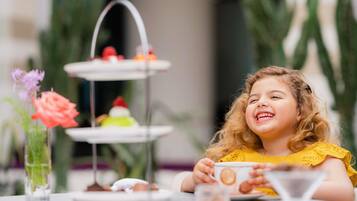 A child at a table with a tiered dessert stand and a vase of flowers.