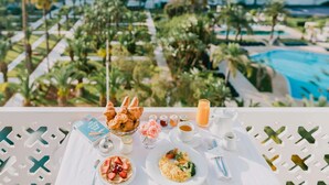 Taula de petit esmorzar amb croissants, un llibre i vista a una piscina i vegetació.
