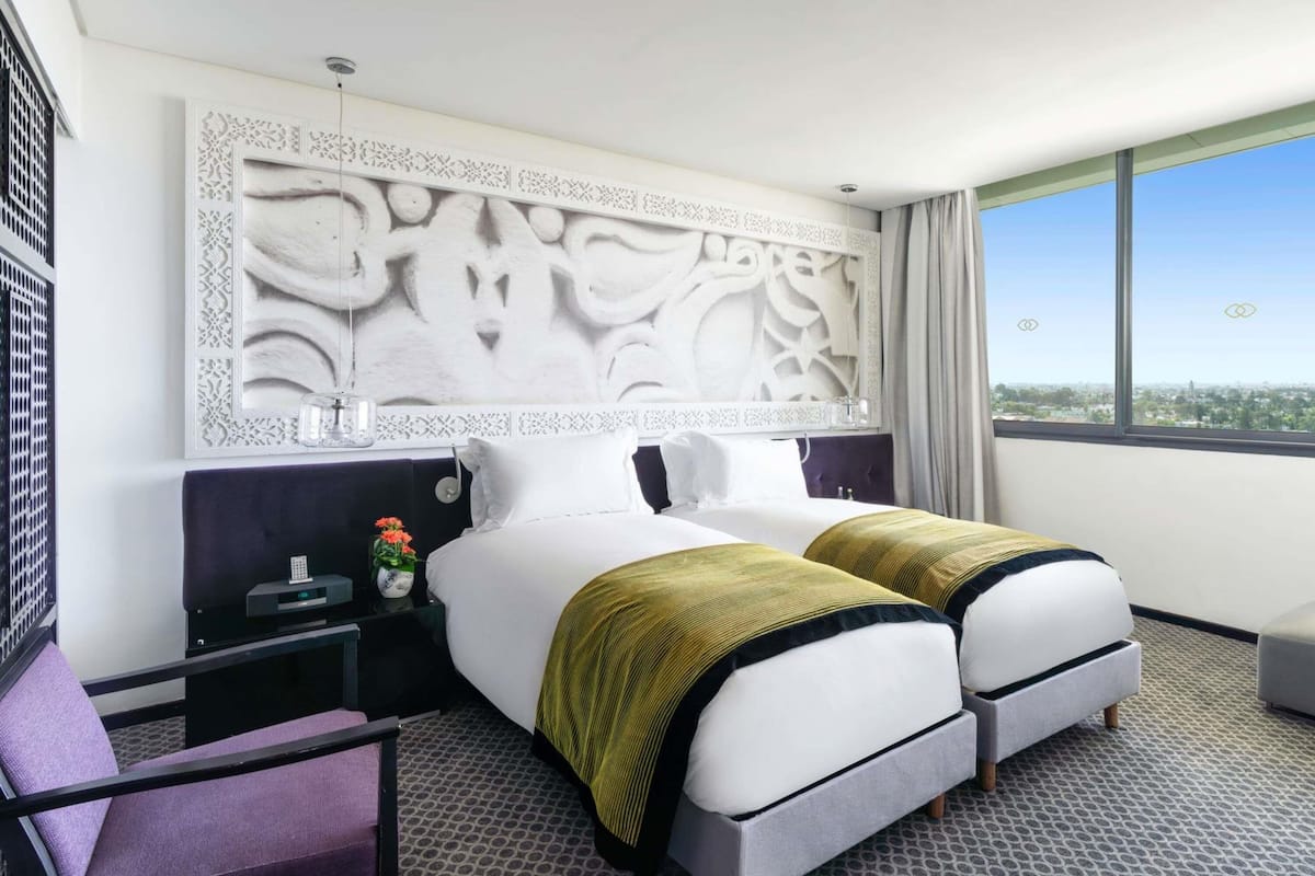 A hotel room with a large bed, two bedside tables, a chair, a decorative headboard, and a city view.